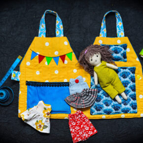 Portable textile dollhouse with rag doll and four outfits laid out on yellow quilted fabric