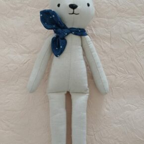 Handmade cream cloth bear soft toy with blue neck scarf on beige background