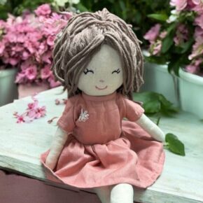 Handmade Daisy rag doll in pink dress sitting on a bench with flowers