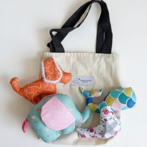 Set of four handmade baby rattles – elephant with crinkle ears, squeaky bird, dog with furry ears and fish with rattle sound – arranged together as a gift kit